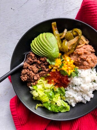 A burrito bowl with lots of veggies next to a red towel