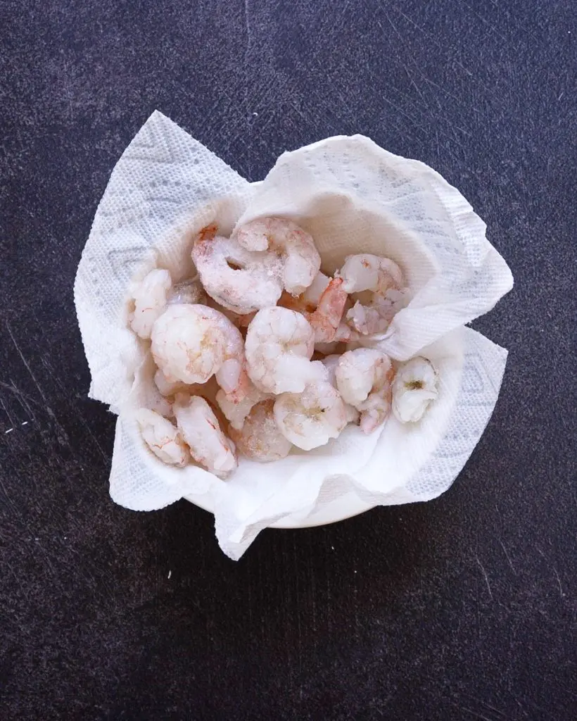 A bowl of raw shrimp on a paper towel.