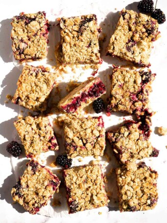 Twelve blackberry crumb bars on a table.