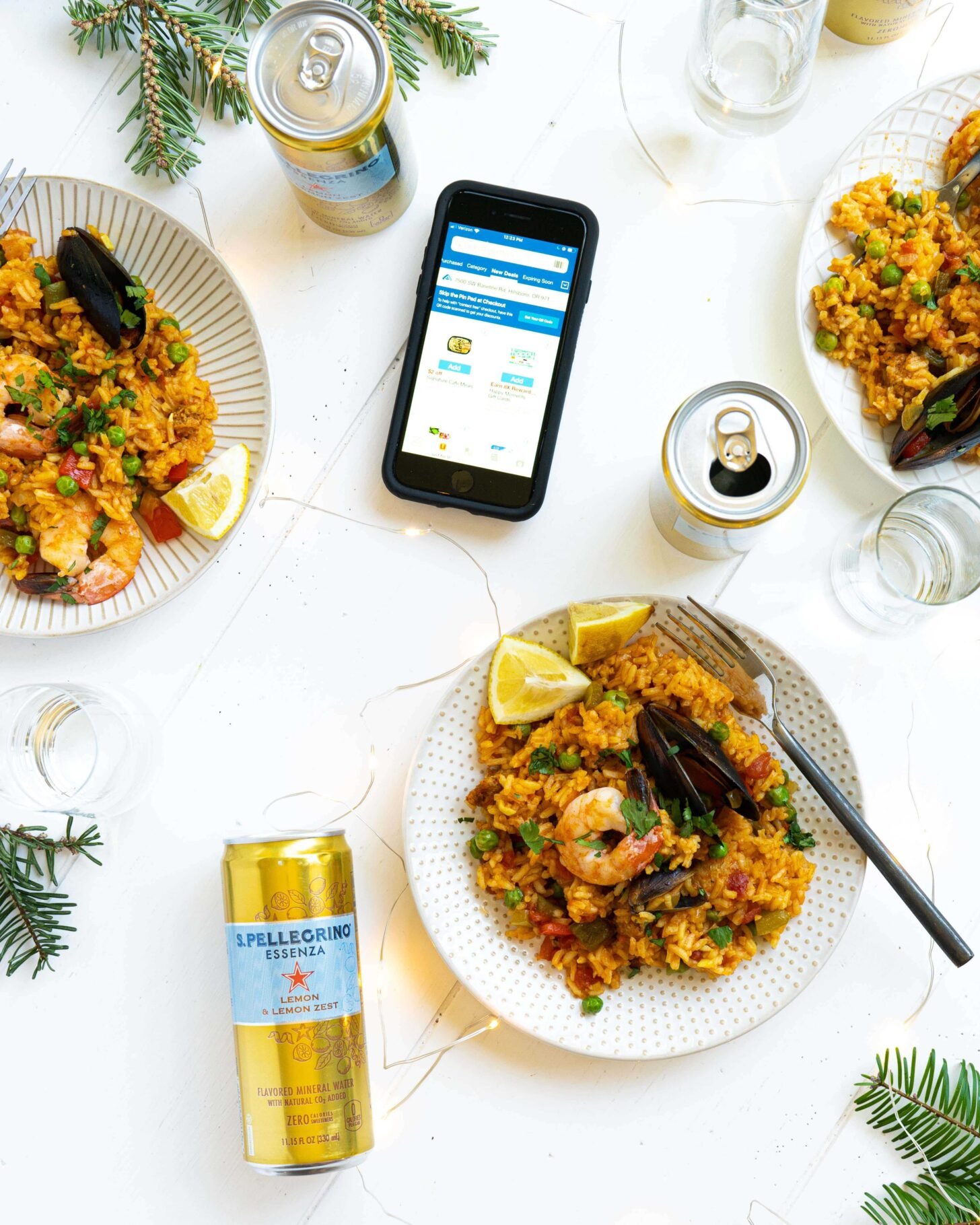Plates of seafood paella next to cans, glasses and a phone