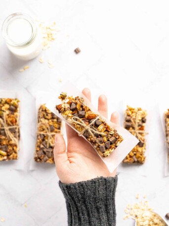 A hand holding a granola bar wrapped in parchment paper and twine