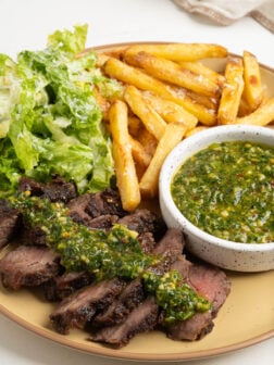A plate of steak and fries with chimichurri.