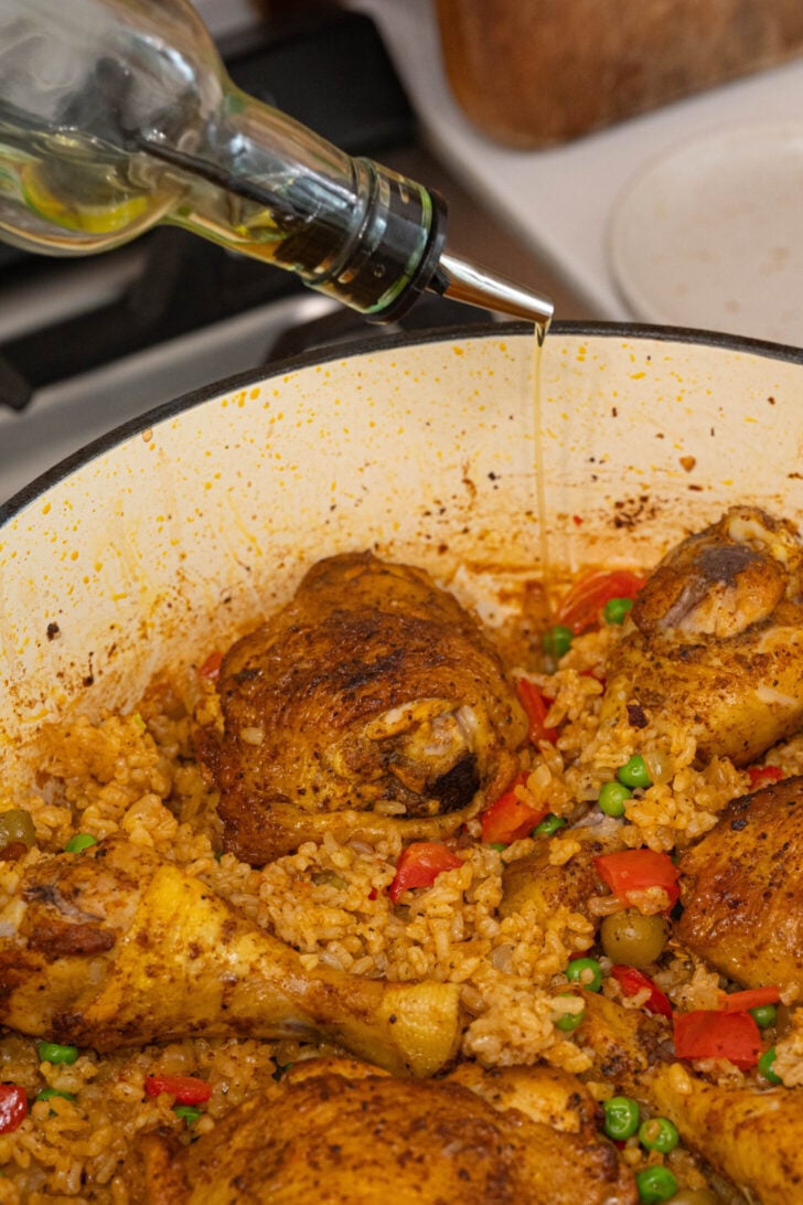 Oil drizzling over a pot of arroz con pollo.
