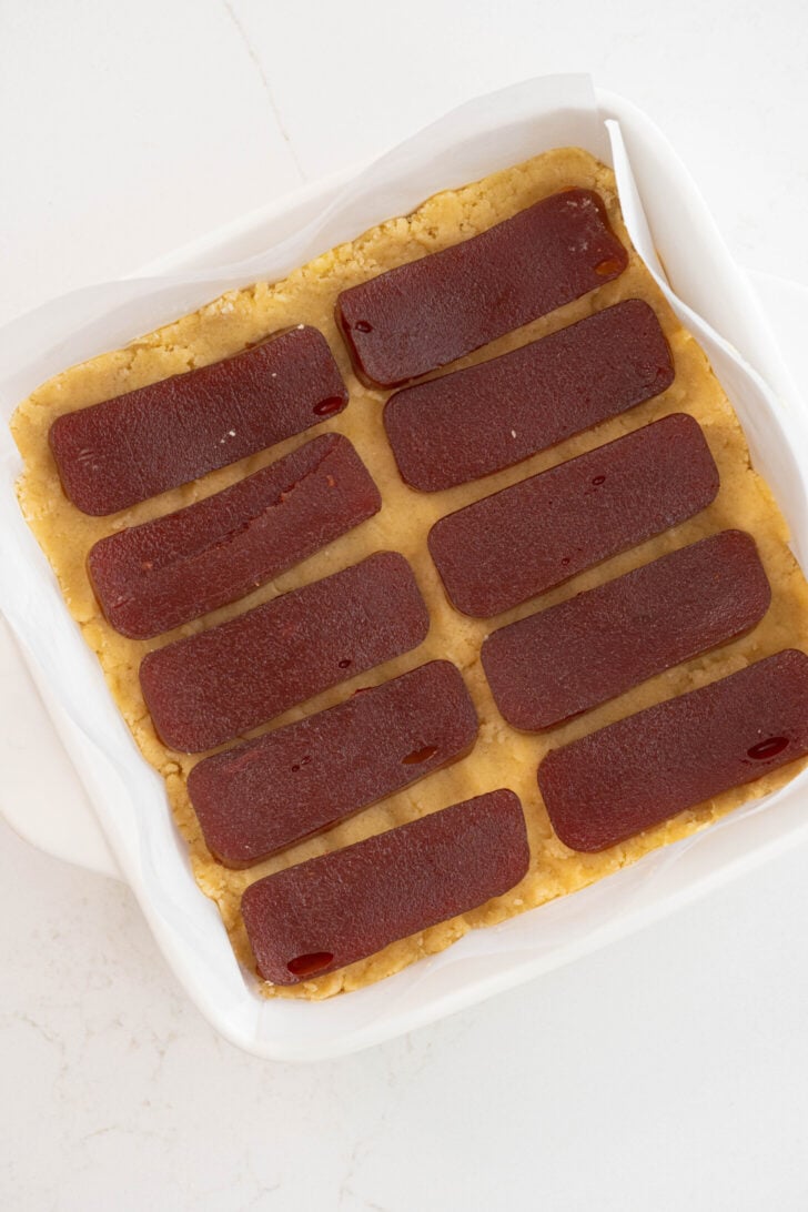 The guava bars are being deposited in the baking dish.
