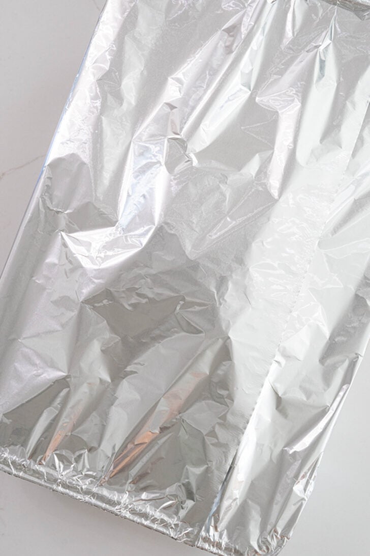 A marinated pork shoulder covered with aluminum.