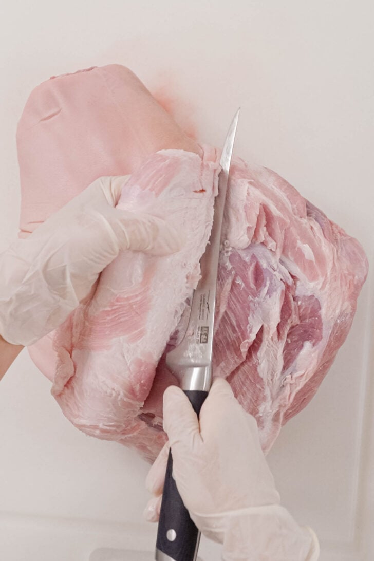 A knife peeling the skin off pork shoulder.