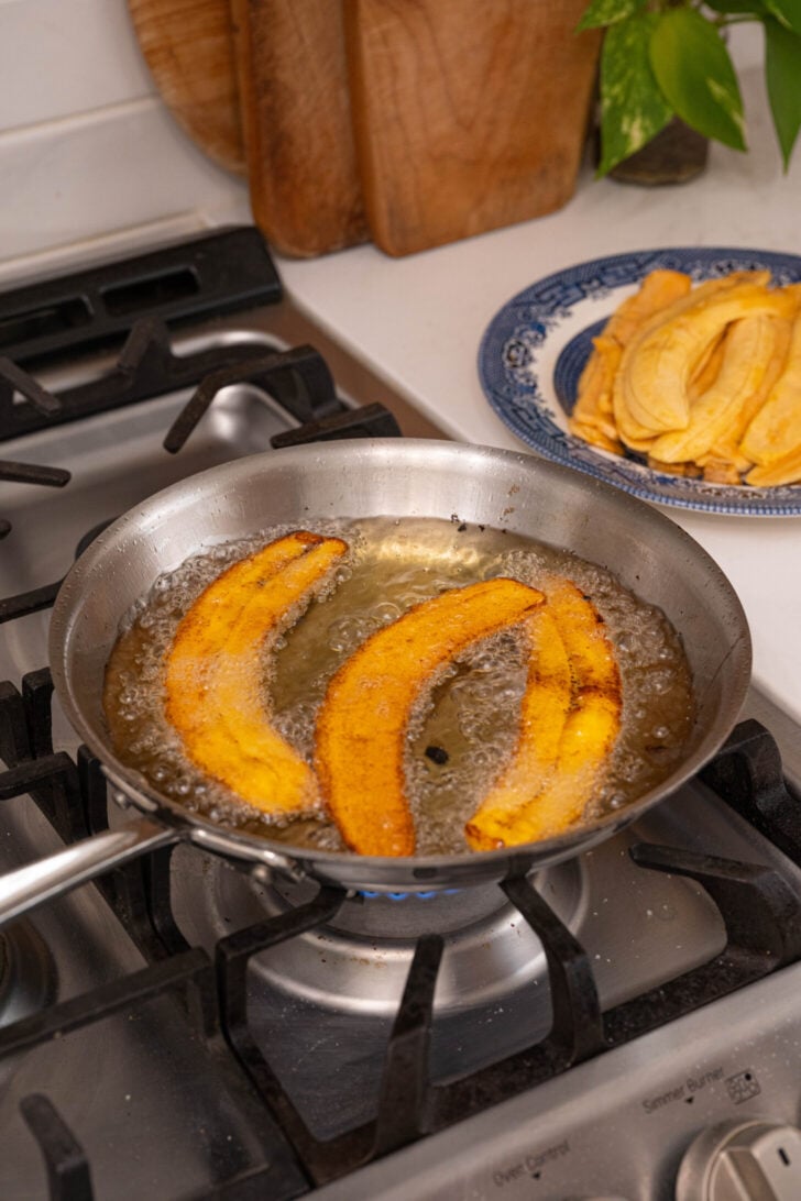 Brown plantain slices frying in oil.