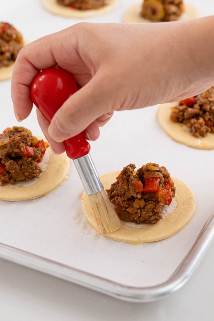 Pastelitos de carne being brushed with egg wash.